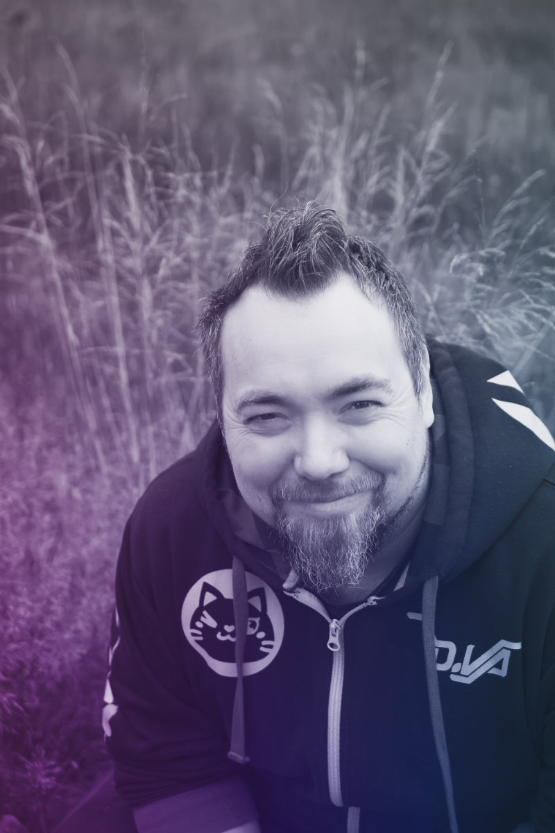 Black & white. Øivind sitting in a grassy field wearing a hoodie with a cat on it.